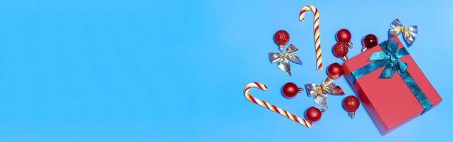 pancarta de hermosas bolas rojas de navidad y un regalo rojo con una cinta verde, con piruletas sobre un fondo azul. concepto de navidad de año nuevo. maqueta festiva plana con espacio de copia foto