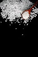 White uncooked rice in wooden spoon on black background. photo