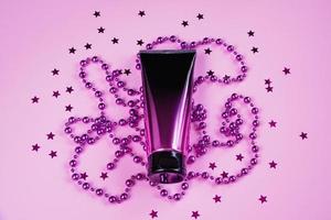 Luxurious black and pink squeeze cosmetic bottles and purple decorations on pastel background. photo