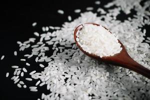 White uncooked rice in wooden spoon on black background. photo