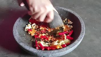 le processus de fabrication d'une sauce chili. une main pulvérise des oignons et des piments dans un pilon sur un mortier en pierre pour faire une sauce chili. video