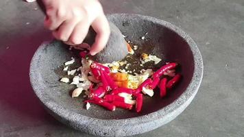 der Prozess der Herstellung einer Chilisauce. Eine Hand pulverisiert Zwiebeln und Chilis in einem Stößel auf einem Steinmörser, um eine Chilisauce herzustellen. video