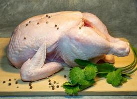 Raw whole chicken on a cutting board on a dark background. Food preparation. Cilantro and peppercorns.  Chicken in spices. Healthy food photo