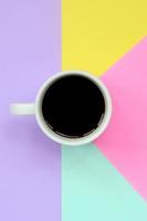 Small white coffee cup on texture background of fashion pastel blue, yellow, violet and pink colors paper in minimal concept photo