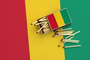 la bandera de guinea se muestra en una caja de cerillas abierta, de la que caen varias cerillas y se encuentra en una bandera grande foto