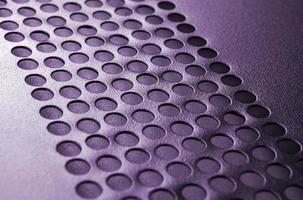 Black metal computer case panel mesh with holes on purple background. Abstract close up photo