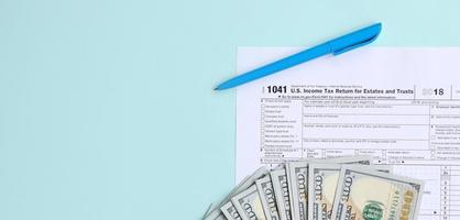 1041 tax form lies near hundred dollar bills and blue pen on a light blue background. US Income tax return for estates and trusts photo