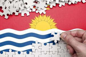 Kiribati flag is depicted on a table on which the human hand folds a puzzle of white color photo