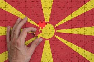 Macedonia flag is depicted on a puzzle, which the man's hand completes to fold photo