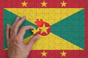 Grenada flag is depicted on a puzzle, which the man's hand completes to fold photo
