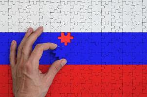 Russia flag is depicted on a puzzle, which the man's hand completes to fold photo