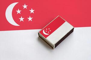 Singapore flag is pictured on a matchbox that lies on a large flag photo