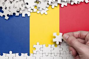 Romania flag is depicted on a table on which the human hand folds a puzzle of white color photo