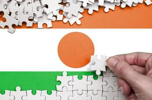 Niger flag is depicted on a table on which the human hand folds a puzzle of white color photo