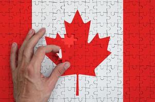 la bandera de canadá está representada en un rompecabezas, que la mano del hombre completa para doblar foto