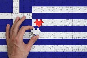 Greece flag is depicted on a puzzle, which the man's hand completes to fold photo