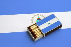 Nicaragua flag is shown in an open matchbox, which is filled with matches and lies on a large flag photo