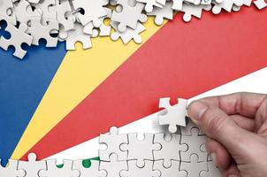 Seychelles flag is depicted on a table on which the human hand folds a puzzle of white color photo