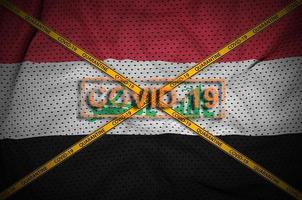 Iraq flag and Covid-19 stamp with orange quarantine border tape cross. Coronavirus or 2019-nCov virus concept photo