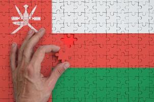 Oman flag is depicted on a puzzle, which the man's hand completes to fold photo