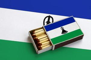 Lesotho flag is shown in an open matchbox, which is filled with matches and lies on a large flag photo