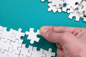 The hand folds a white jigsaw puzzle and a pile of uncombed puzzle pieces lies against the background of the blue surface. Texture photo with space for text