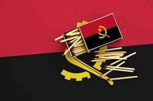 Angola flag is shown on an open matchbox, from which several matches fall and lies on a large flag photo