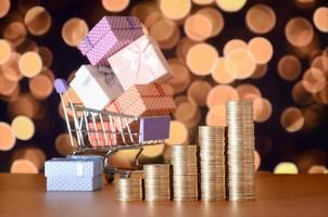 Small red gift box and golden coin stacks on the colored bokeh background photo