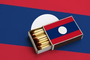 Laos flag is shown in an open matchbox, which is filled with matches and lies on a large flag photo