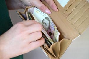 manos femeninas sosteniendo billetes de hryvnia ucraniana en una pequeña bolsa de dinero o billetera foto