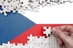 Czech flag is depicted on a table on which the human hand folds a puzzle of white color photo