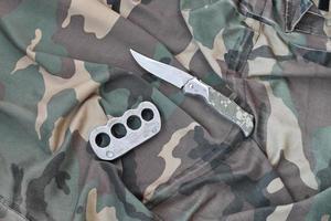 cuchillo y nudillos de latón sobre un fondo de ropa de camuflaje. herramientas para la autodefensa o ataques de delincuentes foto