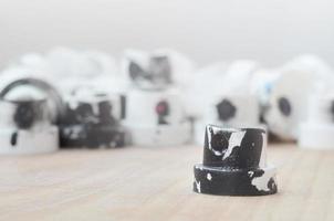 Several plastic nozzles from a paint sprayer that lie on a wooden surface against a gray wall background. The caps are smeared in black paint. The concept of street art and graffiti photo