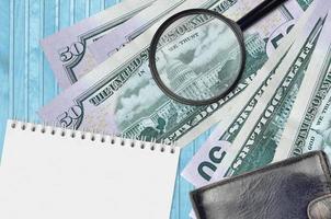 50 US dollars bills and magnifying glass with black purse and notepad. Concept of counterfeit money. Search for differences in details on money bills to detect fake photo