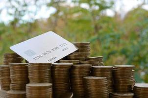 Credit card on big pile of shiny ukrainian old 1 hryvnia coin stacks on blurred green trees background. The concept of money transfer and online banking in Ukraine photo