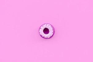 Single small plastic donut lies on a pastel colorful background. Flat lay minimal composition. Top view photo