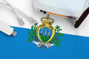 San Marino flag depicted on table with internet rj45 cable, wireless usb wifi adapter and router. Internet connection concept photo