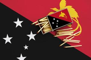 La bandera de papua nueva guinea se muestra en una caja de cerillas abierta, de la que caen varias cerillas y se encuentra en una bandera grande foto