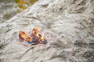 Burning sports sneakers or gym shoes on fire stand on sandy beach coast. Athlete burned out. Physical exertion during training concept photo