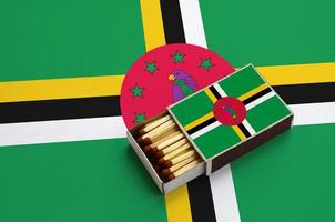 Dominica flag is shown in an open matchbox, which is filled with matches and lies on a large flag photo