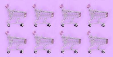 Shopping addiction, shopping lover or shopaholic concept. Many small empty shopping carts perform a pattern on a pastel colored paper background. Flat lay composition, top view photo