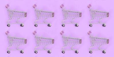 Shopping addiction, shopping lover or shopaholic concept. Many small empty shopping carts perform a pattern on a pastel colored paper background. Flat lay composition, top view photo