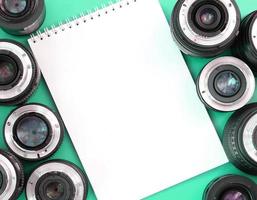 varias lentes fotográficas y un cuaderno blanco yacen sobre un fondo turquesa brillante. copie el espacio foto