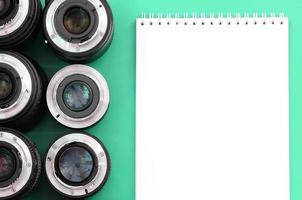 Several photographic lenses and white notebook lie on a bright turquoise background. Copy space photo