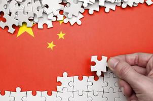 China flag is depicted on a table on which the human hand folds a puzzle of white color photo