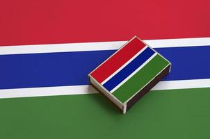 Gambia flag is pictured on a matchbox that lies on a large flag photo