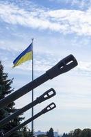 Groups of ancient military guns against the background of the State Flag of Ukraine. Muzzle brake of an artillery gun. Sunny morning sky. Call to stop violence concept. Ukrainian flag. photo