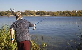 un pescador arrojó una caña giratoria a un lago o río en un día soleado. pesca de orilla. un pescador en la orilla del río sostiene una caña giratoria en la mano. el concepto de descanso del país. artículo de pesca. foto