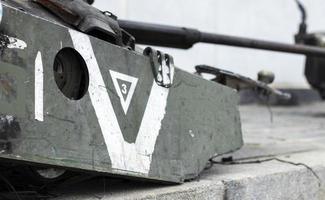 War in Ukraine. Destroyed tank with a torn off turret with a V on it. Broken and burned Russian tanks. Designation sign or symbol in white paint on the tank. Destroyed military equipment. photo