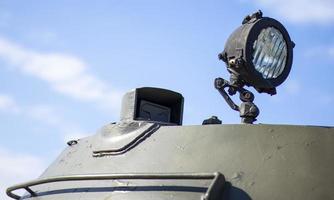 Front headlight of a Soviet battle tank. Very bright searchlight on the tank turret, close-up. Armored infantry fighting vehicle. Fragment of an old armored personnel carrier, khaki headlight. photo